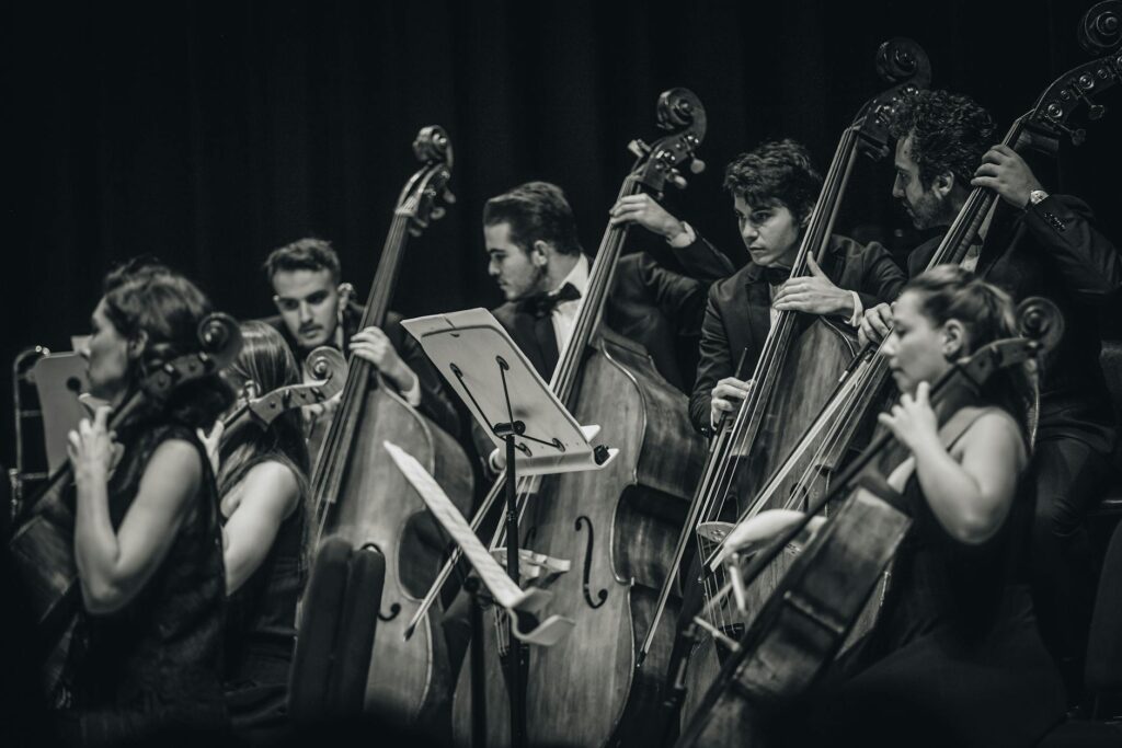 Black and white photo of a classical orchestra performing live, focusing on string musicians.