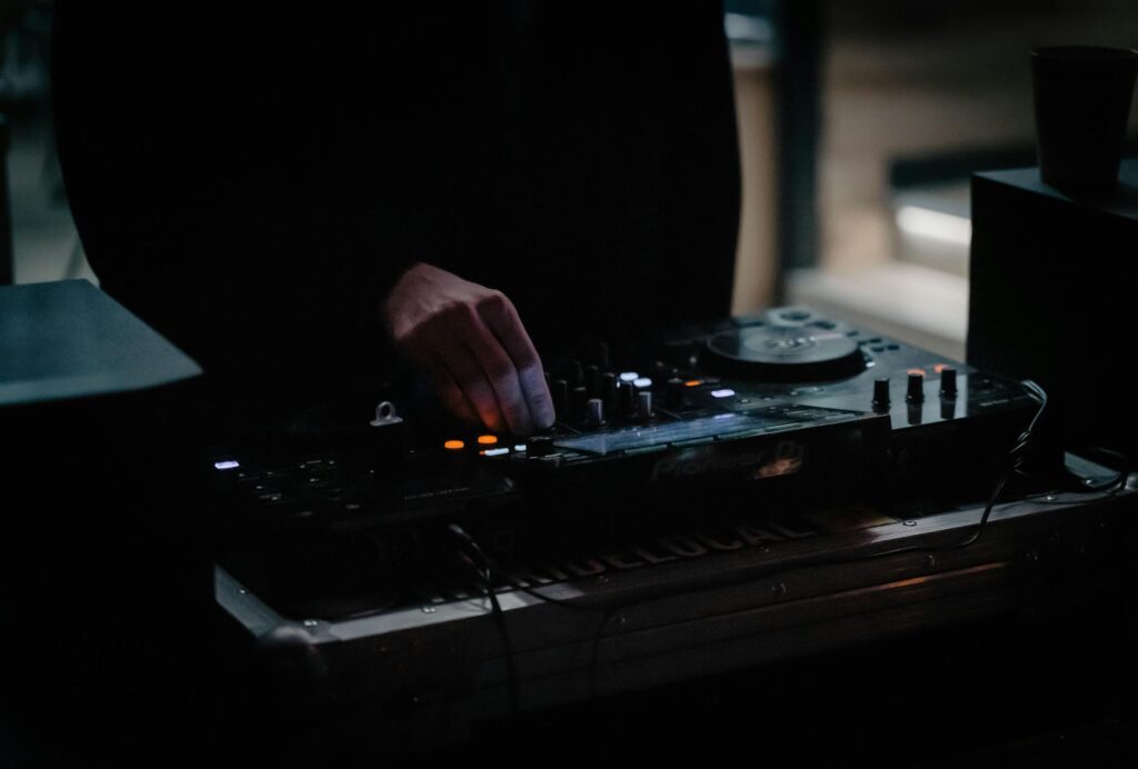 A DJ adjusting a mixer in a dimly lit venue, creating an energetic atmosphere.