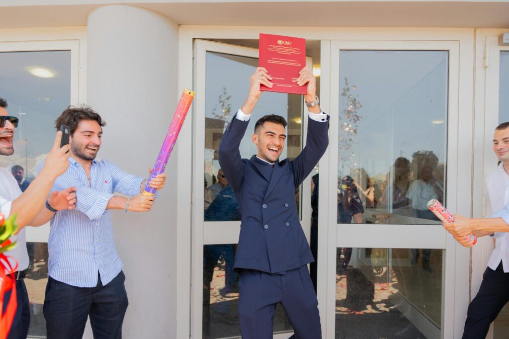 Group of young adults celebrating a graduation in front of a modern building, holding certificates and confetti.