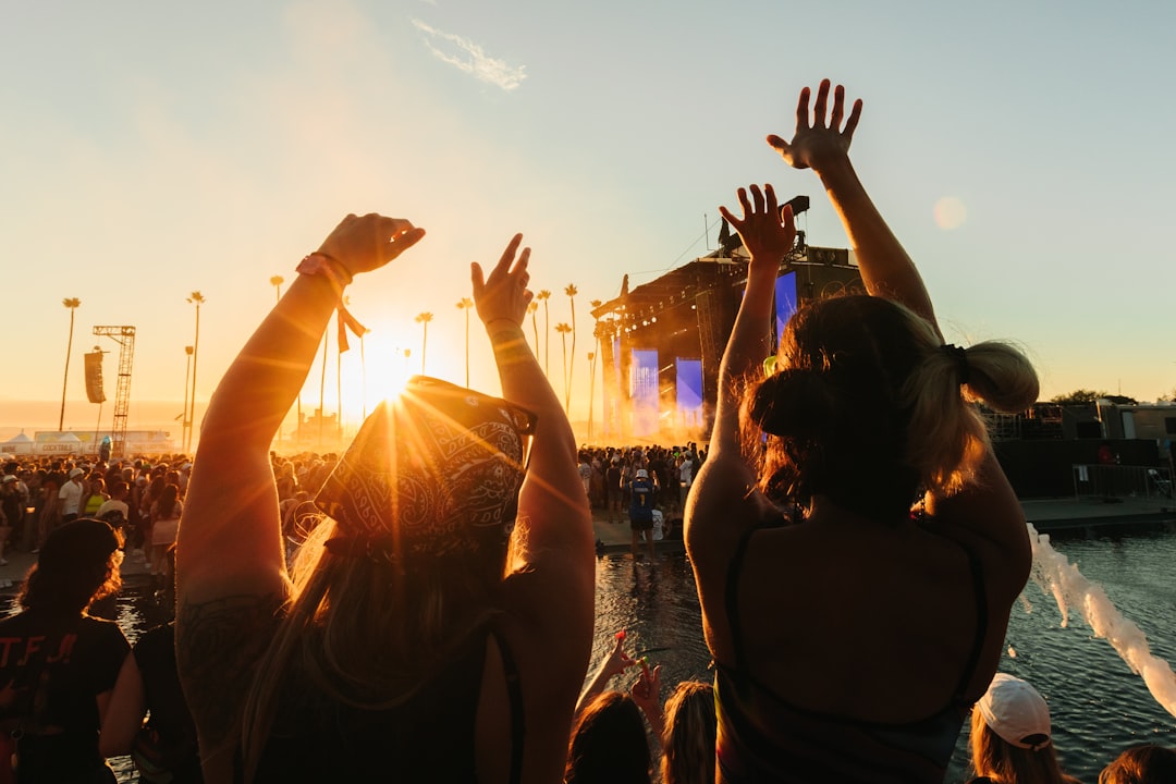 foule les bras levés devant une grande scène de festival de musique en plein air au coucher du soleil